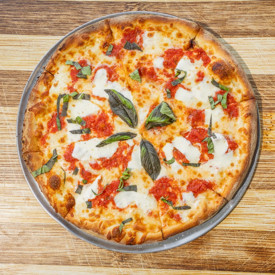 Large Margherita pizza topped with tomato sauce, melted mozzarella, and fresh basil on a metal tray.